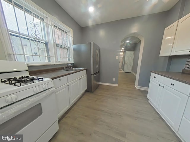 kitchen featuring stainless steel refrigerator, white cabinetry, white gas range, sink, and light hardwood / wood-style floors