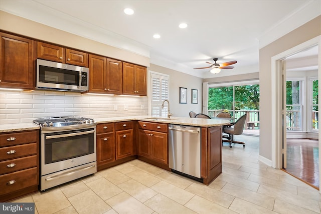 kitchen featuring decorative backsplash, appliances with stainless steel finishes, brown cabinets, a peninsula, and a sink