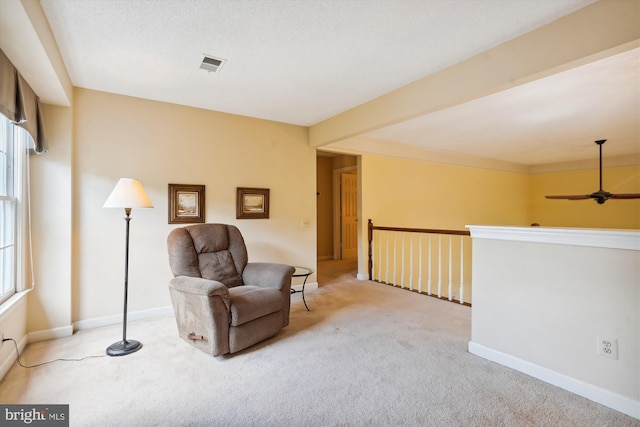 living area featuring light carpet, a ceiling fan, visible vents, baseboards, and beamed ceiling