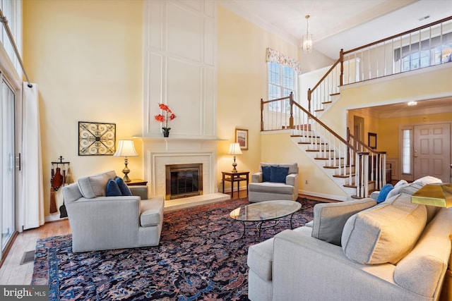 living area featuring visible vents, stairway, a high ceiling, light wood-style floors, and a fireplace