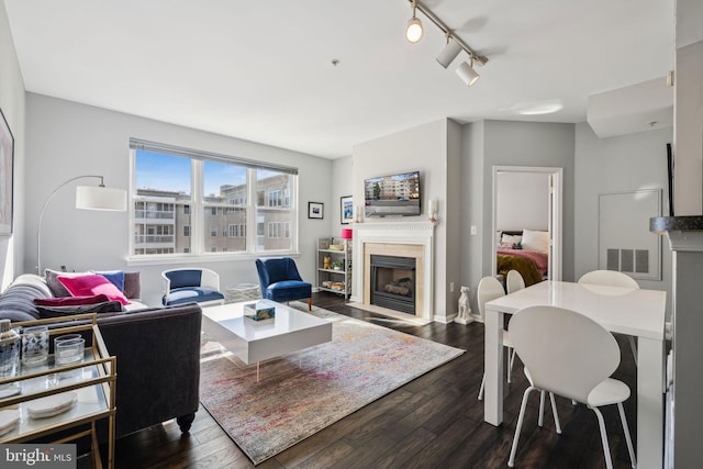 living area with a fireplace with flush hearth, visible vents, track lighting, and dark wood-style floors