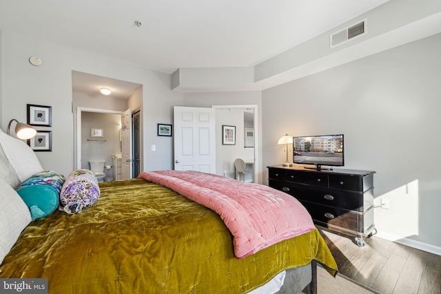 bedroom featuring baseboards, visible vents, ensuite bath, and wood finished floors