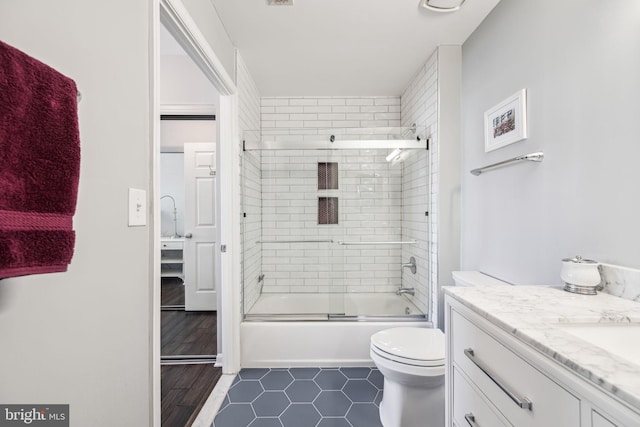 bathroom with toilet, combined bath / shower with glass door, and vanity