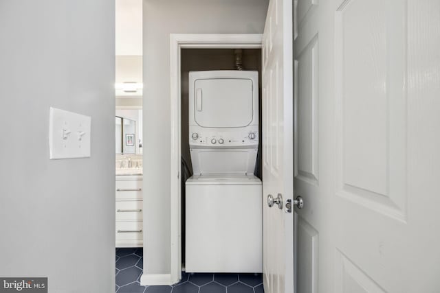 laundry room featuring a sink, laundry area, stacked washer / drying machine, and dark tile patterned flooring