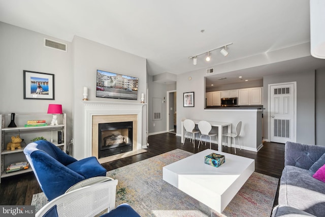 living room featuring dark wood-type flooring, a fireplace with flush hearth, visible vents, and baseboards