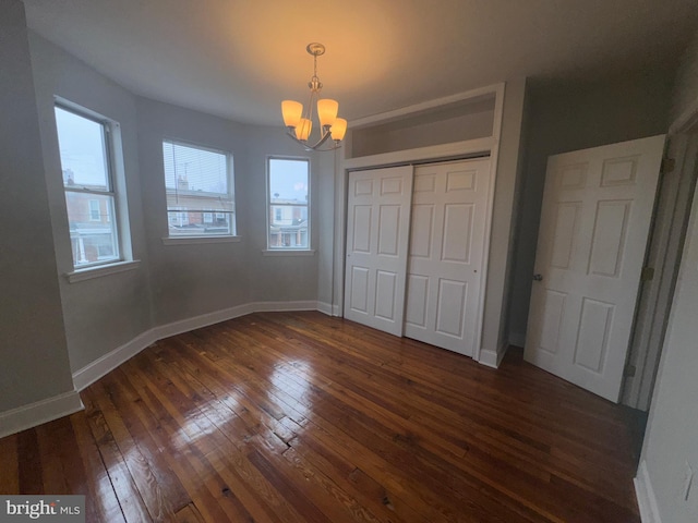 unfurnished bedroom featuring dark wood-type flooring, an inviting chandelier, and a closet