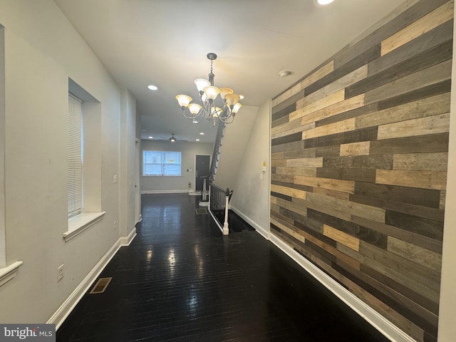 hallway featuring an inviting chandelier, dark hardwood / wood-style floors, and wooden walls