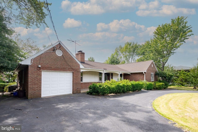 ranch-style house featuring an attached garage, a chimney, aphalt driveway, and brick siding