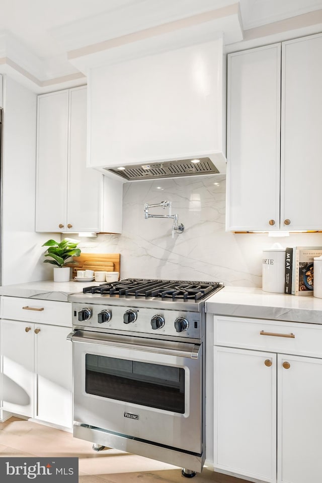 kitchen featuring white cabinetry, backsplash, light stone counters, and premium range