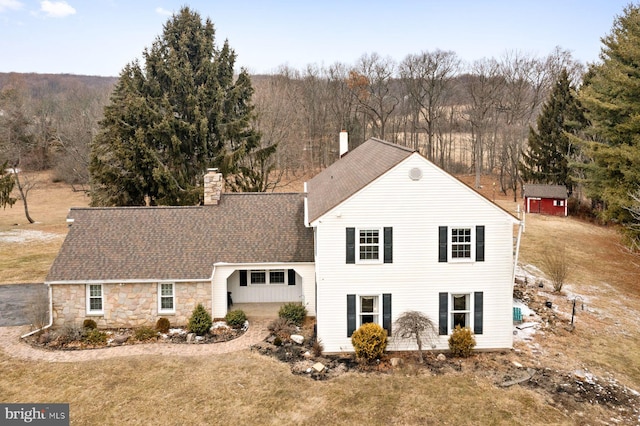 view of front facade with stone siding, a shingled roof, a chimney, and a front yard