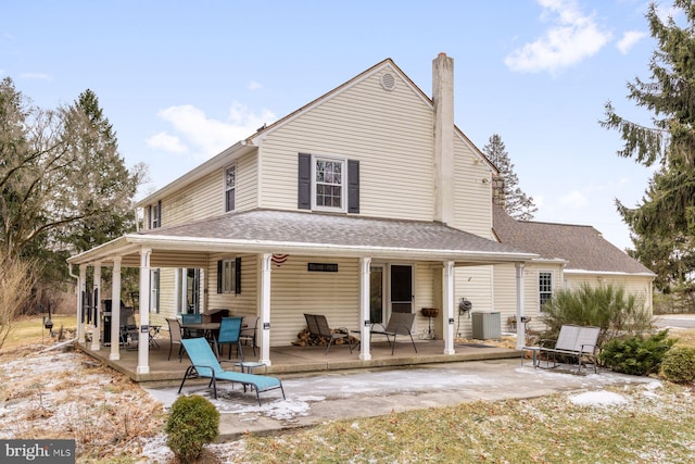 rear view of property featuring a patio area, central AC, a chimney, and roof with shingles