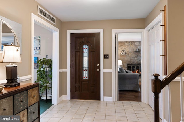 entrance foyer featuring stairway, visible vents, a stone fireplace, and light tile patterned floors