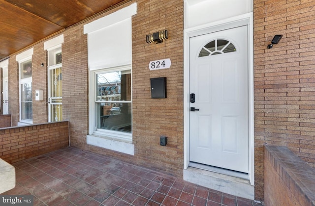 doorway to property featuring a porch and brick siding