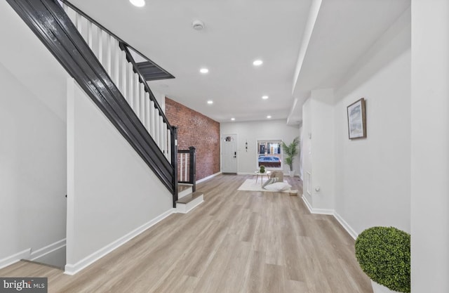 entrance foyer featuring baseboards, brick wall, stairway, and light wood-style floors