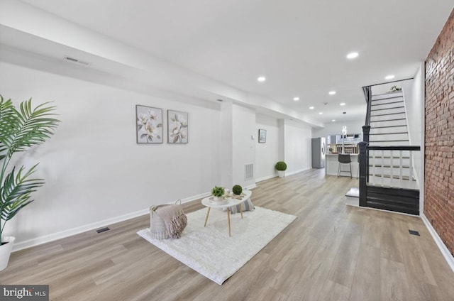 living area with recessed lighting, visible vents, light wood-style floors, brick wall, and stairs