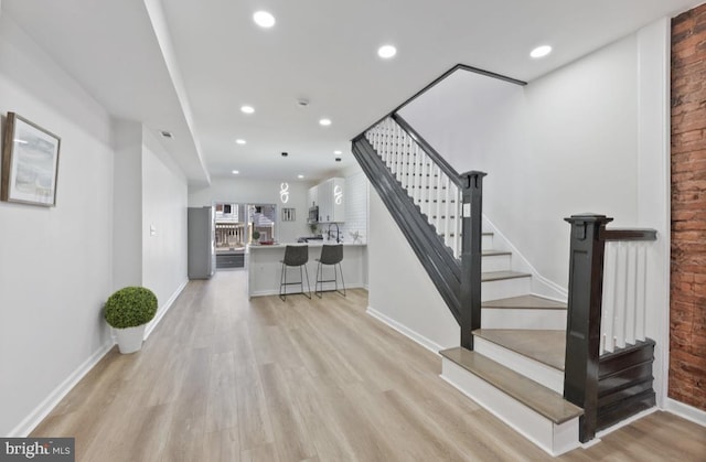 interior space featuring light wood finished floors, brick wall, stairway, and recessed lighting