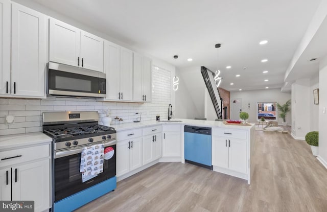 kitchen featuring light wood-style flooring, a peninsula, a sink, open floor plan, and appliances with stainless steel finishes