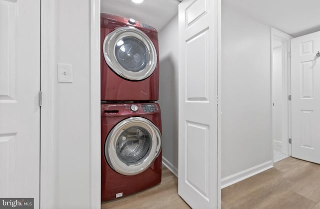 laundry area with laundry area, baseboards, stacked washer / dryer, and wood finished floors