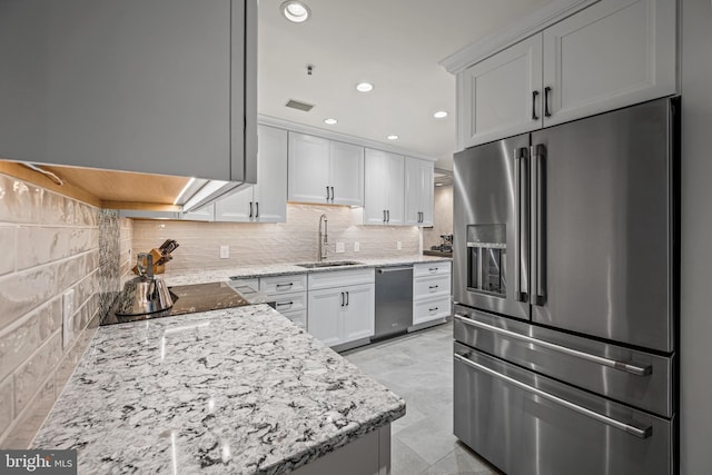 kitchen with light stone counters, stainless steel appliances, tasteful backsplash, white cabinets, and a sink