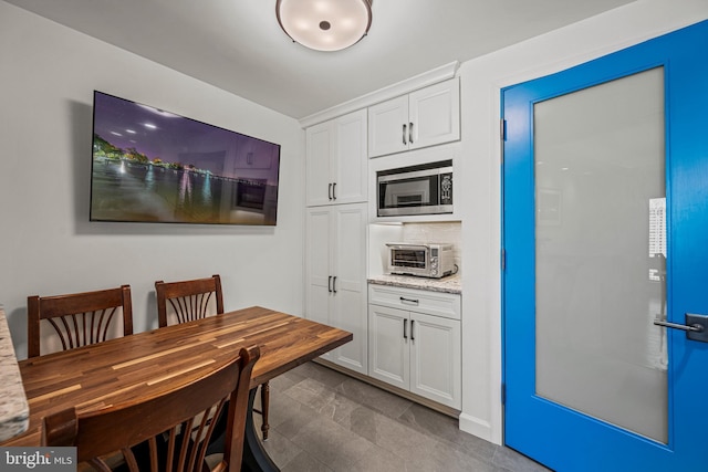 kitchen featuring light stone countertops, a toaster, stainless steel microwave, and white cabinets