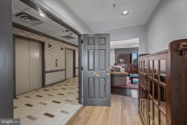 interior space with wallpapered walls, light wood-style flooring, visible vents, and elevator