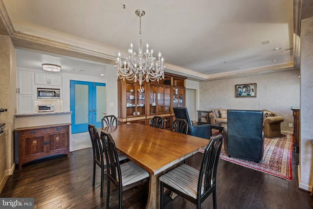 dining space with a raised ceiling, dark wood finished floors, and an inviting chandelier