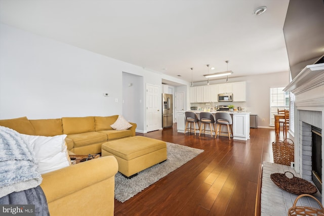 living area featuring a brick fireplace, baseboards, and dark wood-style flooring