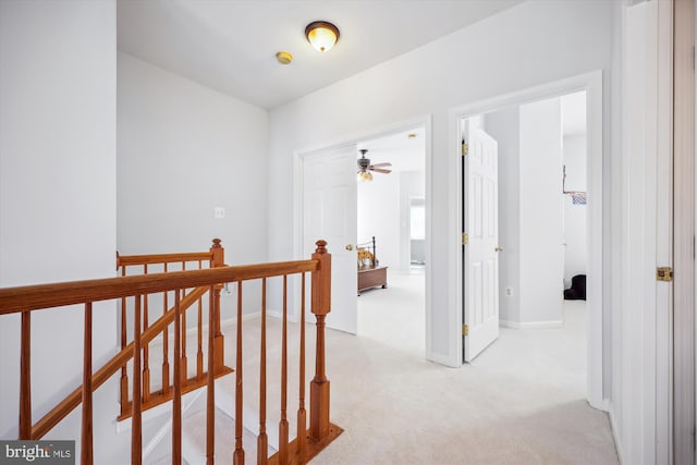 corridor featuring an upstairs landing, light colored carpet, and baseboards