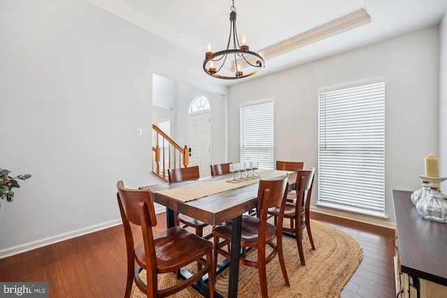 dining area featuring a notable chandelier, ornamental molding, a tray ceiling, and dark wood-style flooring