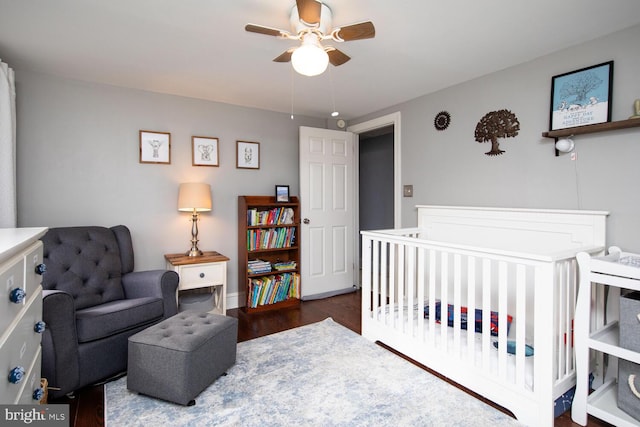 bedroom featuring a nursery area, ceiling fan, and dark hardwood / wood-style floors