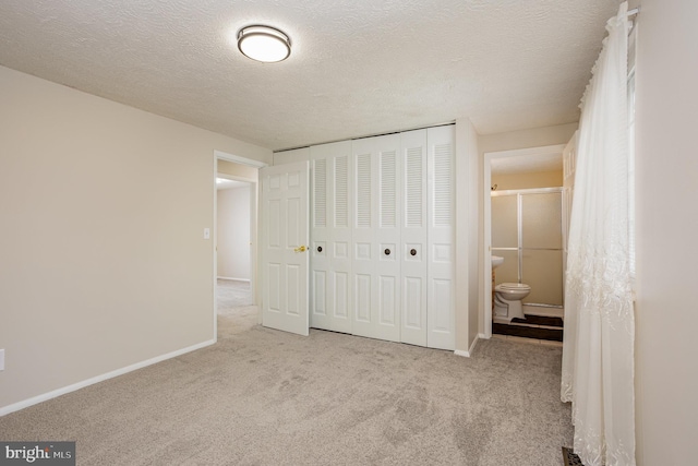 unfurnished bedroom featuring light carpet, a closet, a textured ceiling, and ensuite bathroom