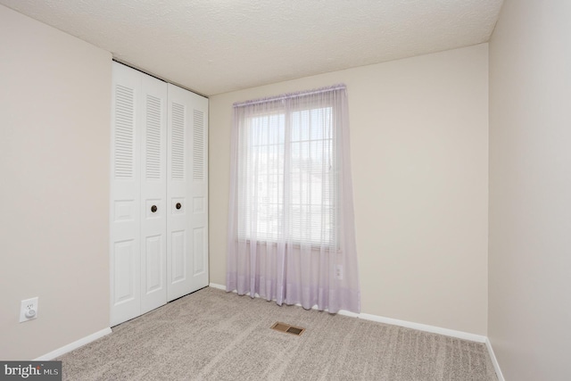 unfurnished bedroom with light carpet, a closet, and a textured ceiling