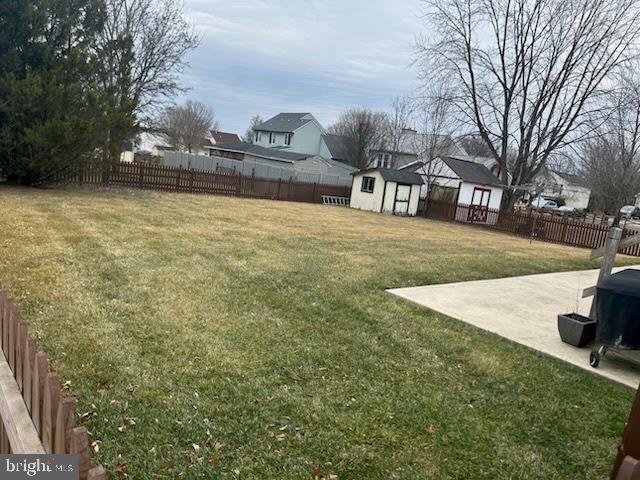 view of yard featuring a fenced backyard, a storage unit, a patio, and an outbuilding