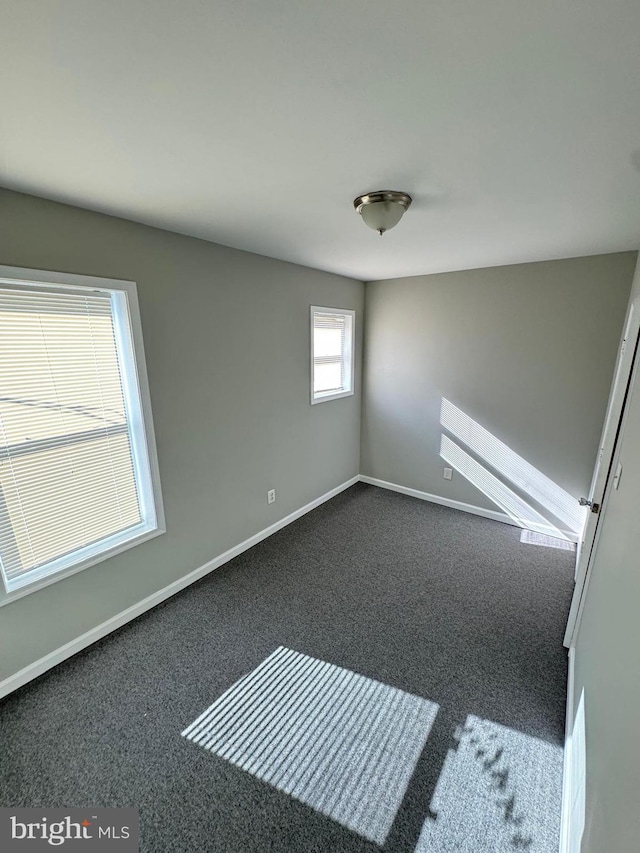 spare room with dark carpet and baseboards