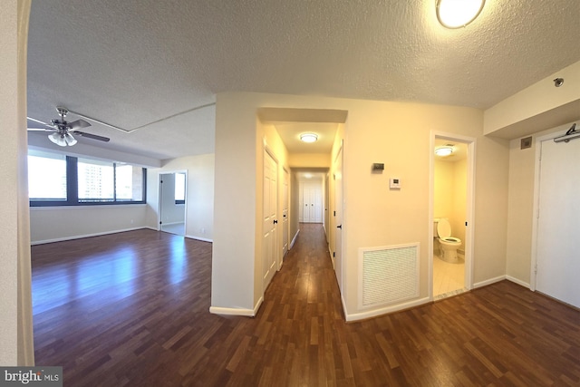 hall with baseboards, visible vents, dark wood finished floors, and a textured ceiling