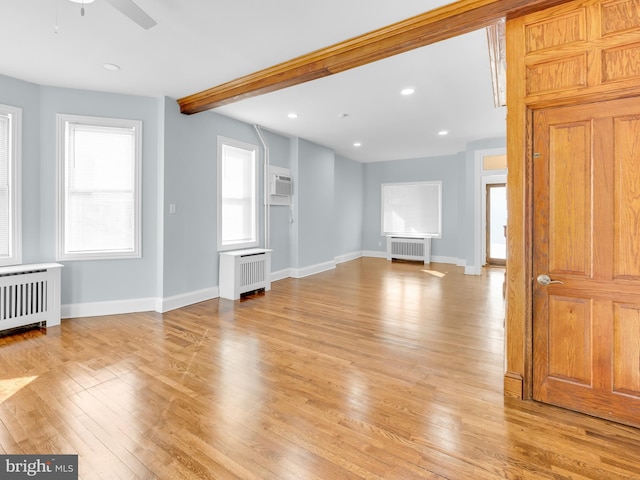 unfurnished room featuring beam ceiling, a wall unit AC, radiator heating unit, and light wood-type flooring