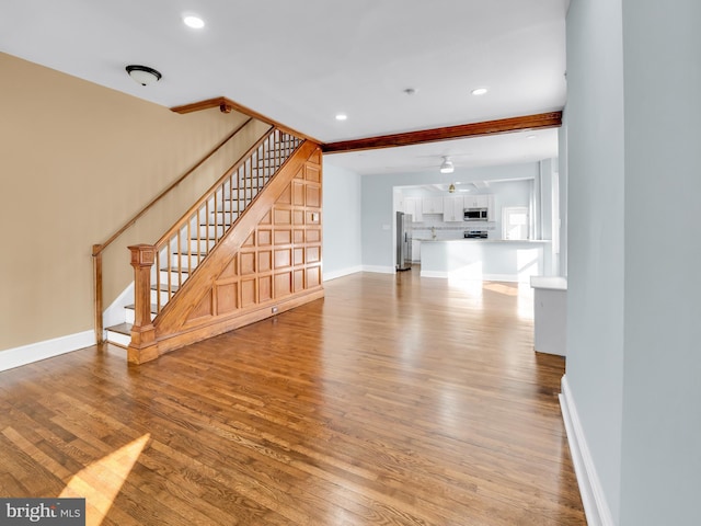 unfurnished living room with beamed ceiling, hardwood / wood-style floors, and ceiling fan