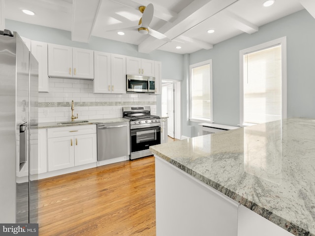 kitchen with appliances with stainless steel finishes, white cabinetry, sink, light stone counters, and light wood-type flooring