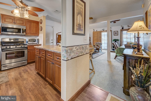 kitchen with stainless steel appliances, light stone countertops, ceiling fan, and light hardwood / wood-style flooring