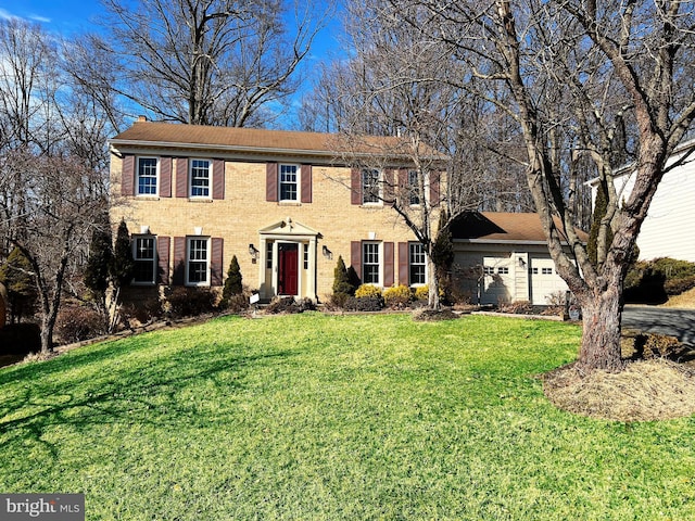 colonial home with brick siding, a chimney, a front lawn, and a garage