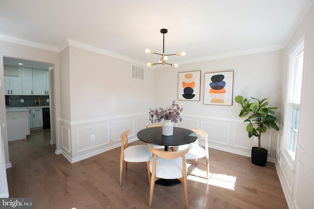 dining room featuring a notable chandelier, wood finished floors, visible vents, and ornamental molding