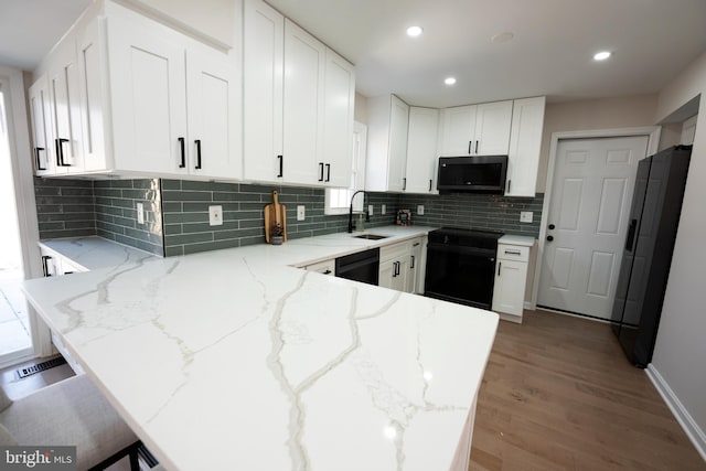 kitchen with light stone counters, a peninsula, white cabinets, black appliances, and a sink