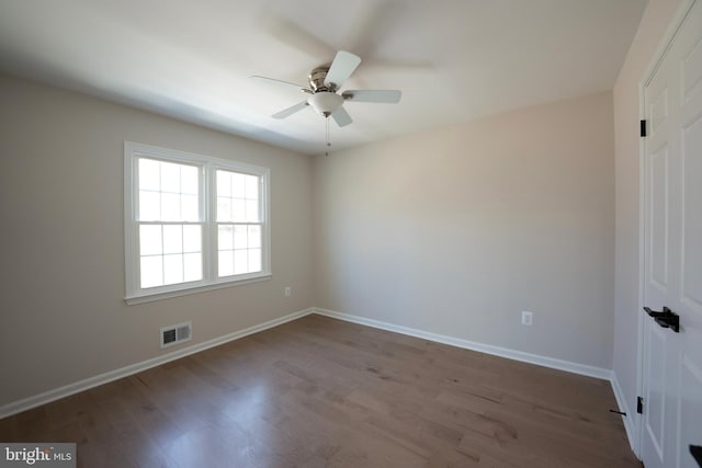 empty room featuring dark wood finished floors, visible vents, a ceiling fan, and baseboards