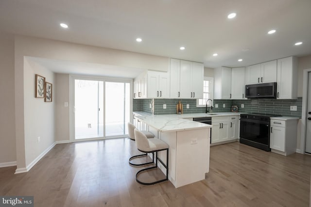 kitchen with tasteful backsplash, black electric range oven, white cabinetry, and a peninsula