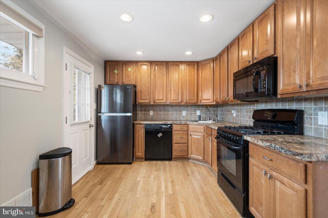 kitchen with light wood-type flooring, backsplash, brown cabinets, dark stone counters, and black appliances