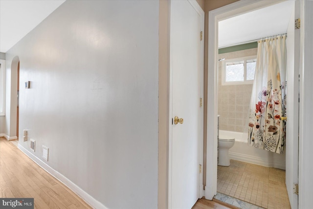 hallway featuring arched walkways, light wood-style flooring, visible vents, and baseboards