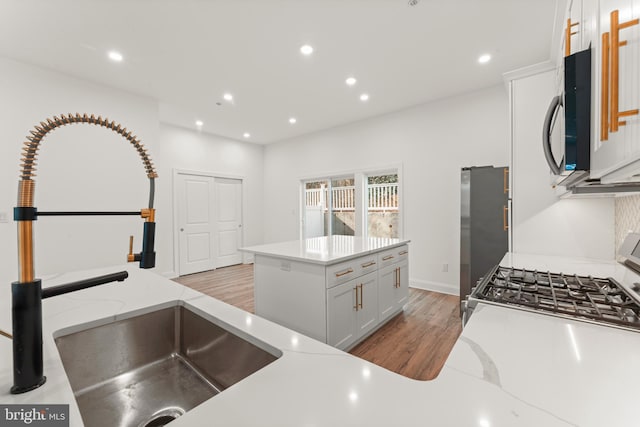 kitchen featuring sink, white cabinetry, light hardwood / wood-style flooring, stainless steel fridge, and a kitchen island