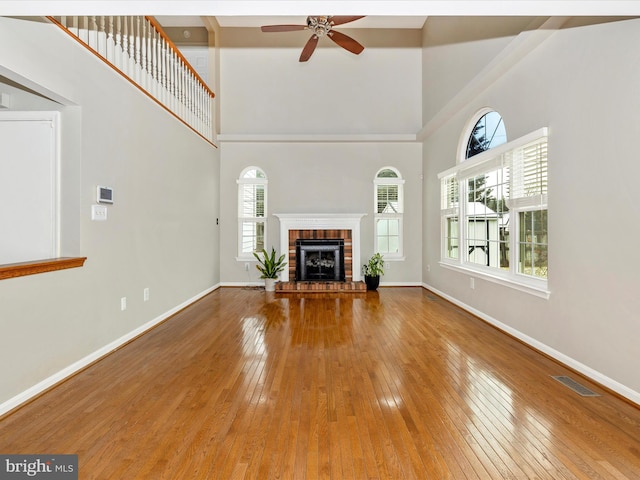 unfurnished living room with hardwood / wood-style flooring, a brick fireplace, a high ceiling, and ceiling fan