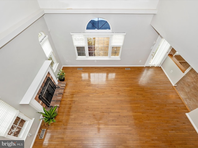 unfurnished living room with hardwood / wood-style flooring, a brick fireplace, and a towering ceiling