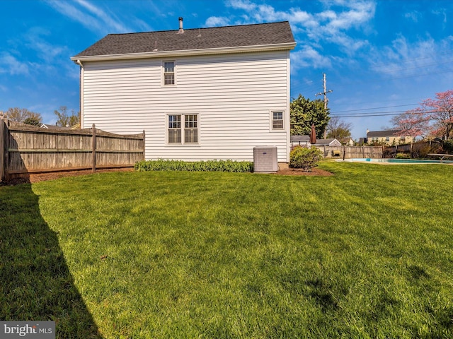 rear view of property with central AC, a fenced in pool, and a lawn